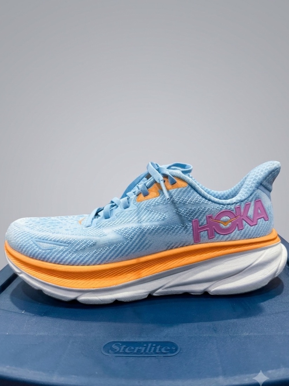 Hoka Women’s Clifton 9 Light Blue and Orange Running Shoe with Pink Logo.